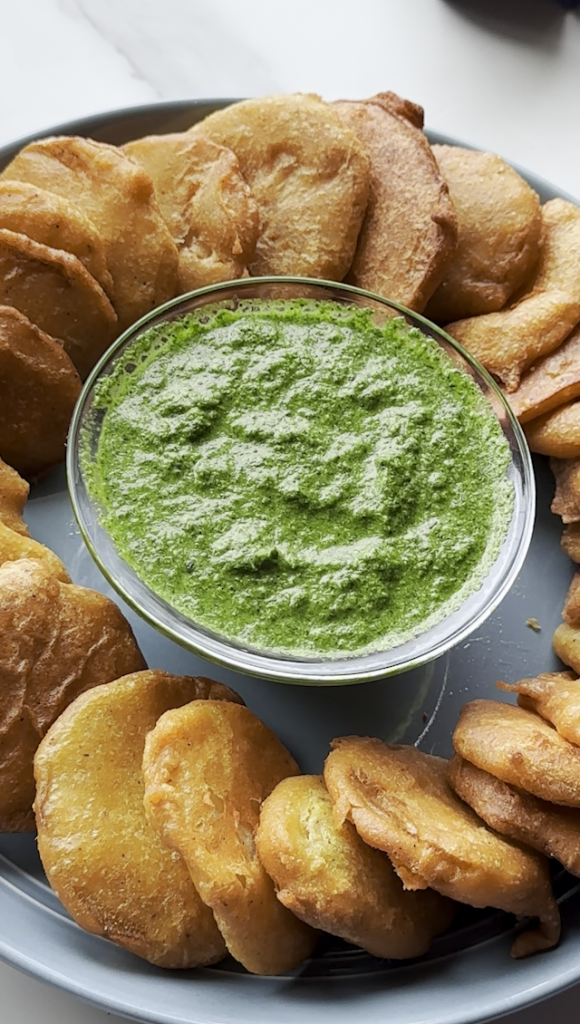 a plate full of Afghan Pakawra, which is a veggie fritter. this one is potato with a bowl of cilantro chutney